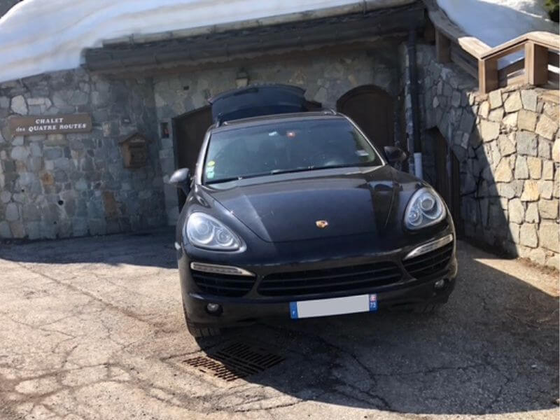 Porsche Cayenne noire avec chauffeur devant un chalet en station de ski en Savoie